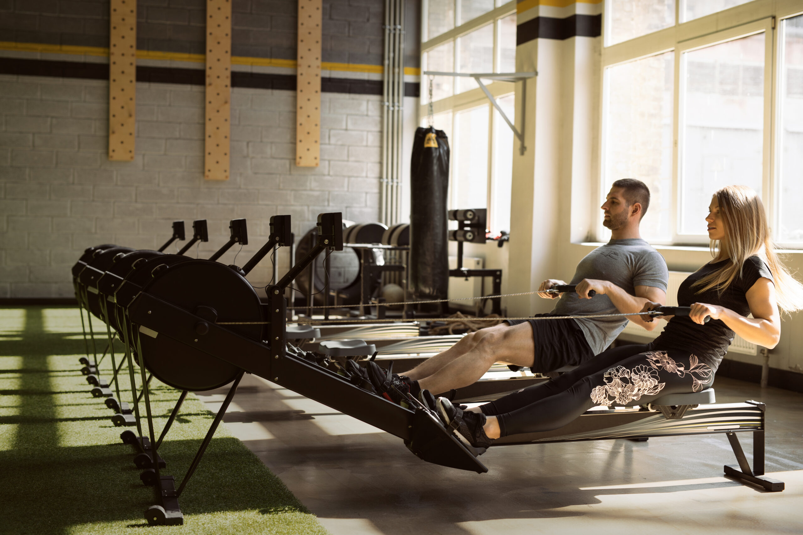 Man And Woman Training On Rowing Machines In Gym Together